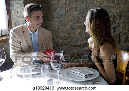 Young man giving a present to young woman at restaurant table View Large Photo Image Stock Image - Young man giving a present to young woman at restaurant table. Fotosearch