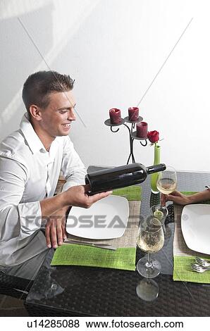 Stock Photo - Young man pouring wine for young woman at restaurant table. Fotosearch