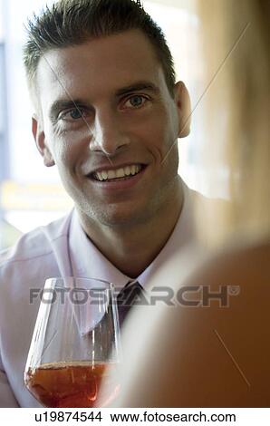 Picture - Young man sitting with a glass of orange wine and young woman. Fotosearch