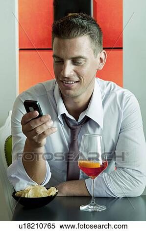 Stock Photography - Young man sitting with a glass of orange wine and mobile phone. Fotosearch