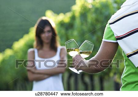 Stock Photo - Young woman in vineyard, man bringing glasses of white wine. Fotosearch