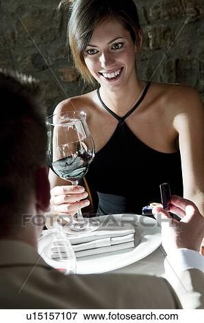 Stock Photo - Young woman smiling at young man giving her a ring. Fotosearch
