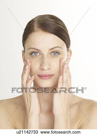 Stock Image - Woman is massaging her face under her eyes. Fotosearch
