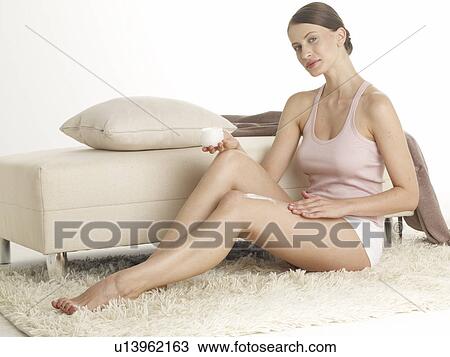 Stock Image - Woman sitting on the floor is putting lotion on thigh. Fotosearch