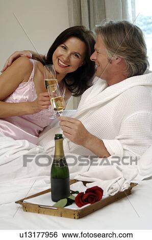 Stock Photograph - Couple in bed drinking sparkling wine. Fotosearch