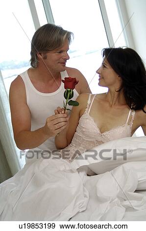 Stock Photo - Couple in bed, man is holding a rose. Fotosearch