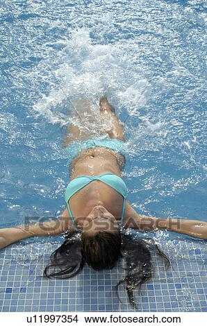 Picture - Woman doing backstrokes at the side of a swimming pool. Fotosearch