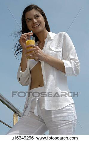 Stock Photograph - Woman dressed in white is enjoying a drink under a blue sky. Fotosearch