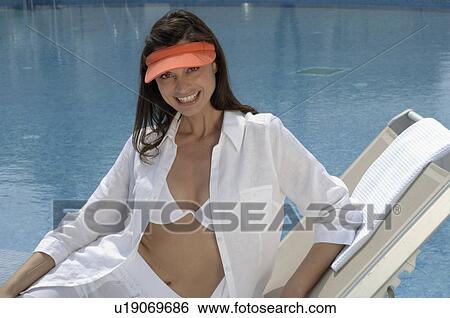 Stock Photograph - Woman with white clothes and a cap at the swimming pool. Fotosearch