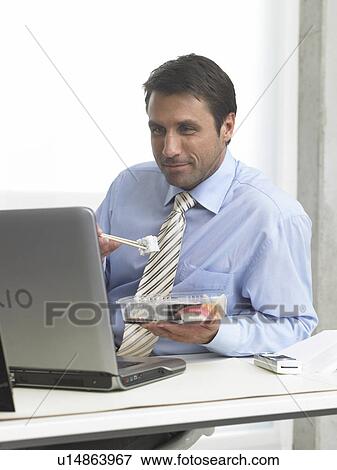 Stock Photo - Business man is eating sushi at his desk. Fotosearch
