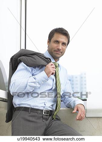 Stock Image - Business man with his jacket over his shoulder is standing at the window. Fotosearch