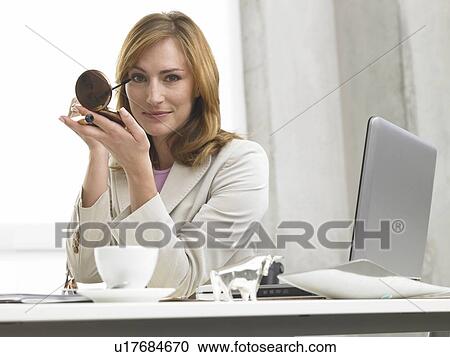 Stock Image - Business woman with make up sitting at her desk. Fotosearch
