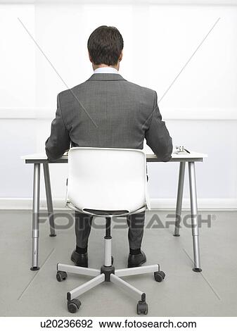 Stock Image - Rearview of a business man sitting at his desk. Fotosearch