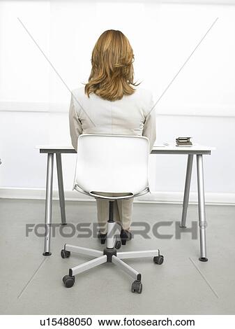 Stock Image - Rearview of a business woman sitting at her desk. Fotosearch