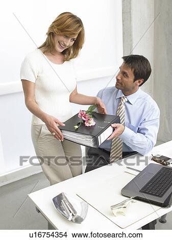 Picture - Woman is giving a file with a rose on it to her colleg. Fotosearch