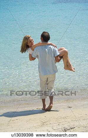 Stock Photo - Couple on the beach - man is carrying woman. Fotosearch