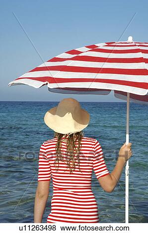 Stock Photo - Woman wearing a hat and a red and white sunshade in the water. Fotosearch