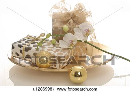 Stock Photo - Gifts on a plate decorated with christmas balls and orichd blossoms. Fotosearch