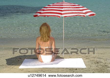 Woman sitting on the beach under a sunshade - back view View Large Photo Image Picture - Woman sitting on the beach under a sunshade - back view. Fotosearch
