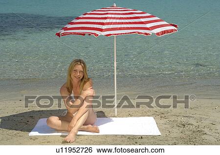Stock Photograph - Woman sitting on the beach under a sunshade. Fotosearch