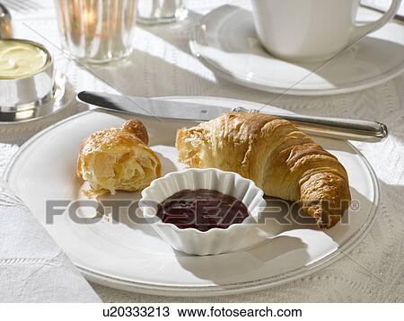 Stock Image - Breakfast table place setting with a croissant and jam. Fotosearch
