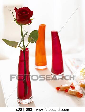 Stock Image - Orange and red glass vases with single rose blossom. Fotosearch