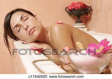 Stock Image - Woman in bath tub with petals, closing her eyes. Fotosearch