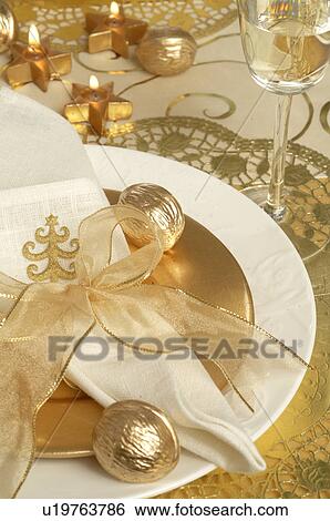 Stock Photograph - Christmas table place setting, napkin tied with a golden ribbon and golden walnuts. Fotosearch