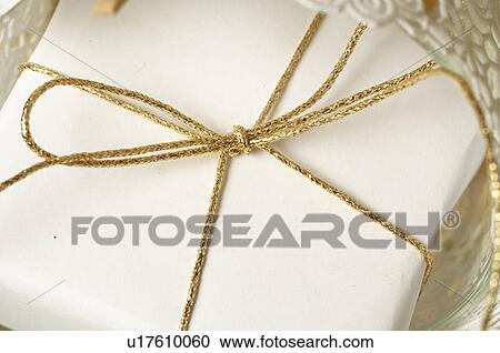 Stock Image - White wrapped Christmas gift tied with a golden ribbon. Fotosearch