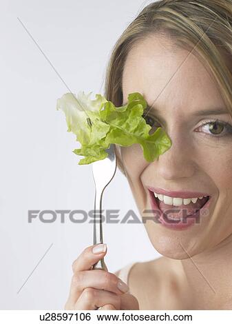 Stock Photograph - Woman is eating salad, holding fork in front of the face. Fotosearch