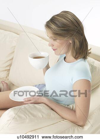 Stock Image - Woman on the sofa drinking a cup of tea. Fotosearch