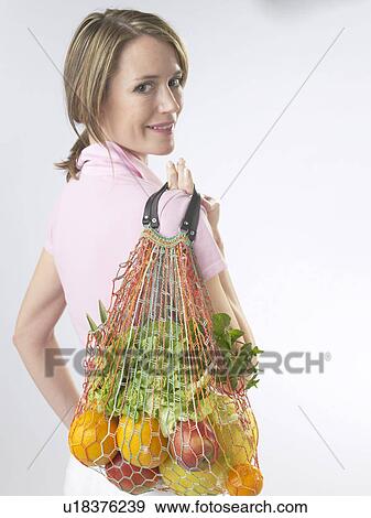 Stock Photo - Woman with fruit and vegetables in a string bag. Fotosearch