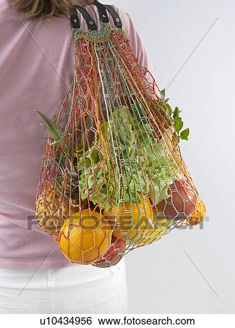 Stock Photograph - Woman with fruit and vegetables in a string bag. Fotosearch
