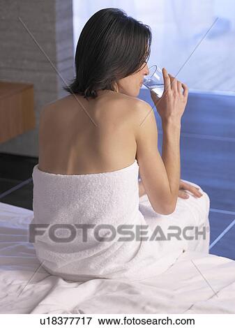 Stock Photo - Woman sitting on a massage table and drinking water. Fotosearch