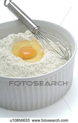 Stock Image - Flour, egg and a whisk in a bowl. Fotosearch