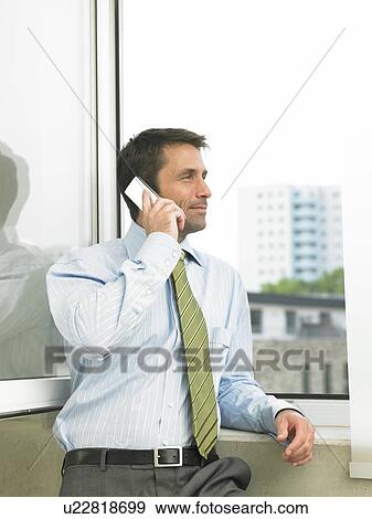 Business man is standing and phoning at the window View Large Photo Image Stock Photo - Business man is standing and phoning at the window. Fotosearch