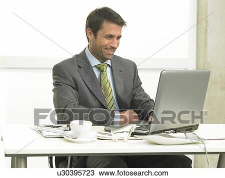 Stock Image - Business man on his desk working with his laptop. Fotosearch