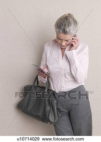 Stock Photo - Phoning senior adult with flight ticket and bag. Fotosearch