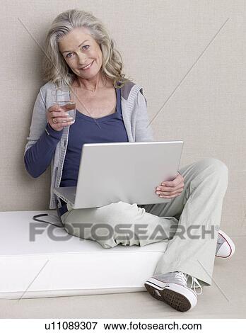 Stock Photo - Senior Adult with a laptop is holding a glass of water. Fotosearch