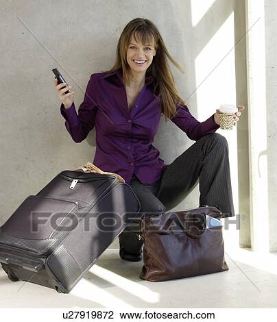 Woman with a trolley and a bag is holding a cell phone and a coffee cup in her hands View Large Photo Image Stock Image - Woman with a trolley and a bag is holding a cell phone and a coffee cup in her hands. Fotosearch
