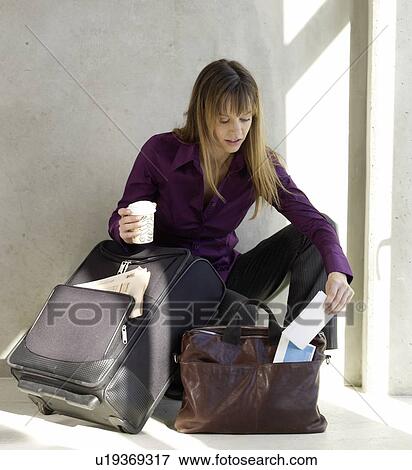 Stock Photo - Woman with a trolley and a bag is taking her flight tickets. Fotosearch