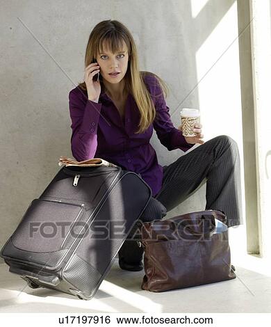 Stock Photograph - Woman with a trolley and a bag is phoning with a cell phone. Fotosearch