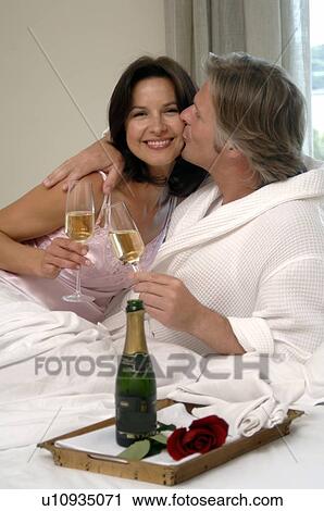 Stock Image - Couple in bed drinking sparkling wine. Fotosearch