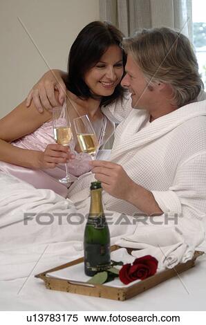 Stock Photography - Couple in bed drinking sparkling wine. Fotosearch