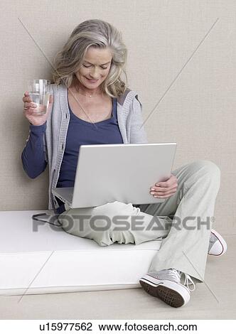 Stock Image - Senior adult in sports clothing with laptop and glass of water. Fotosearch