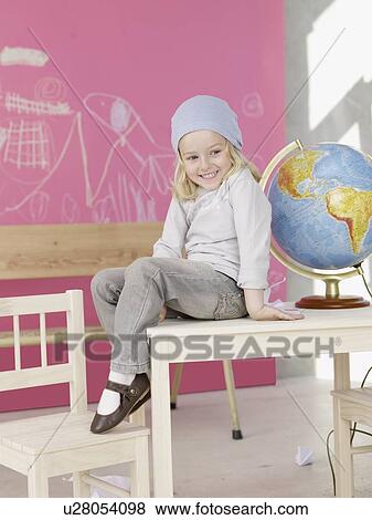 Stock Photo - Blond girl wearing a headscarf sitting on the table next to globe. Fotosearch