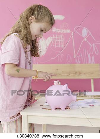 Girl is putting money in a piggy bank View Large Photo Image Stock Photo - Girl is putting money in a piggy bank. Fotosearch