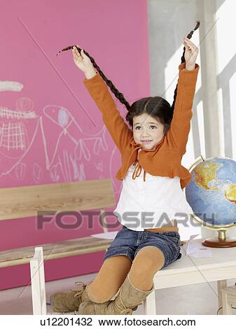 Stock Image - Girl sitting on the table next to globe lifting her plait. Fotosearch