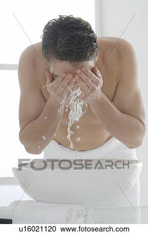 Stock Image - Man standing in front of a washbowl washing his face. Fotosearch