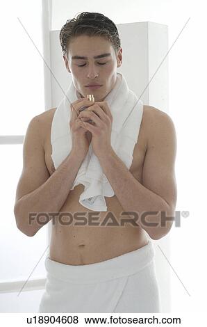 Stock Photo - Man standing in front of a washbowl smelling on a small perfume bottle. Fotosearch
